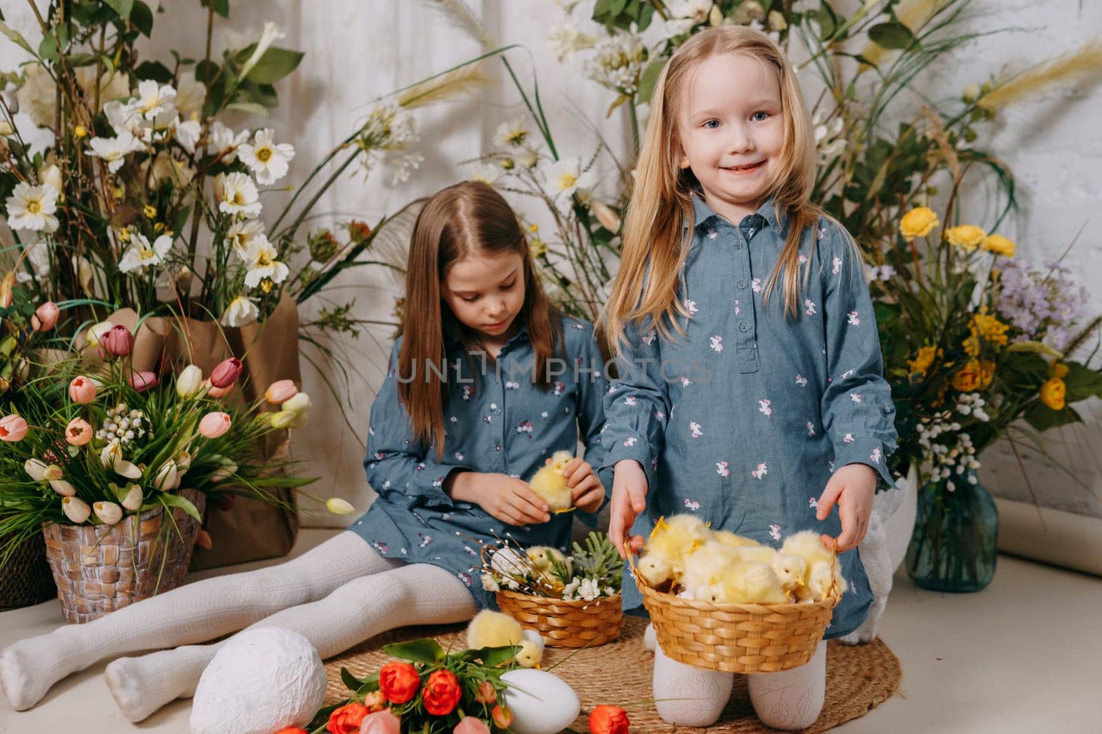 Two girls in a beautiful Easter photo zone with flowers, eggs, chickens and Easter bunnies. Happy Easter holiday. by Annu1tochka