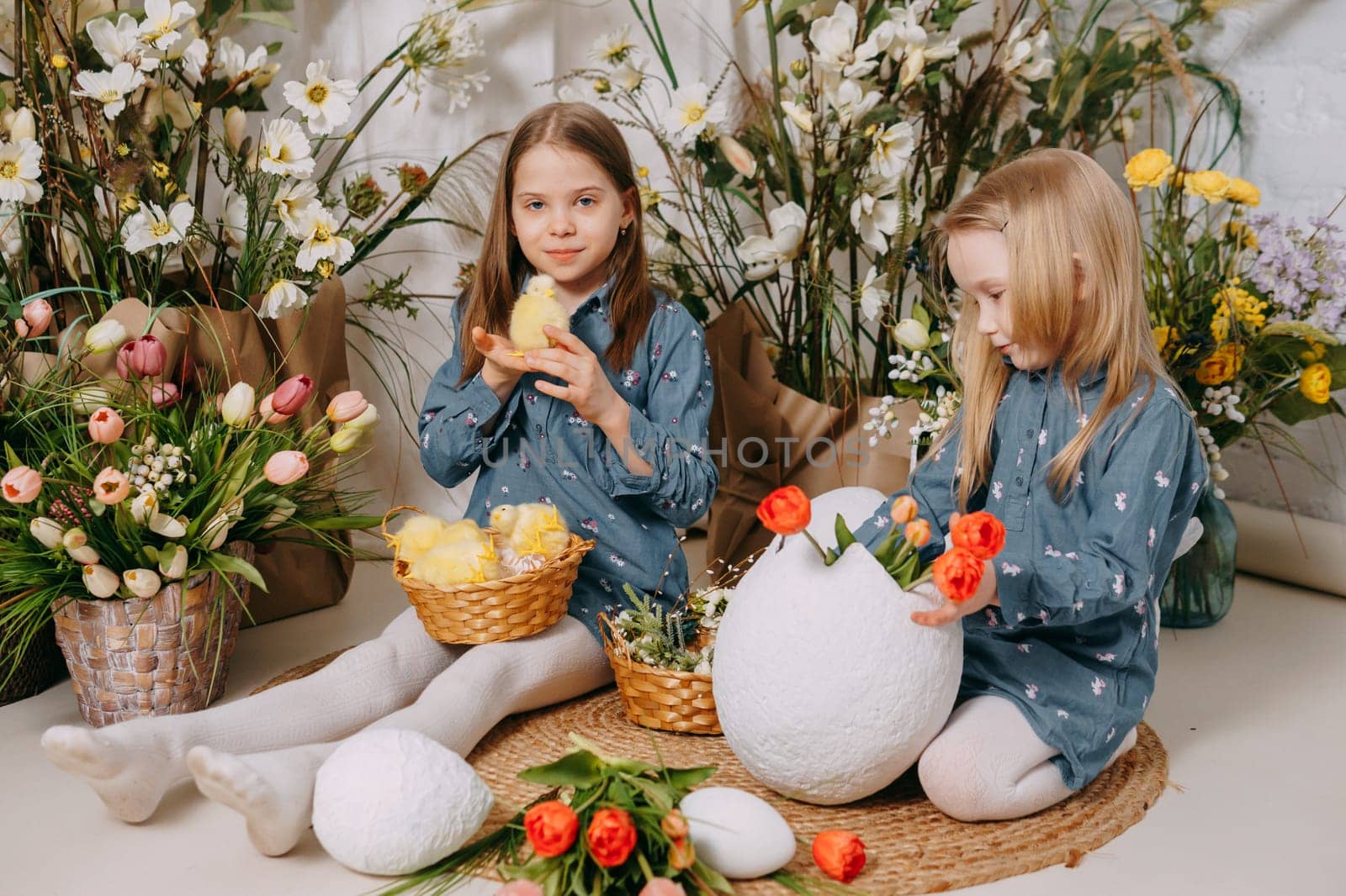 Two girls in a beautiful Easter photo zone with flowers, eggs, chickens and Easter bunnies. Happy Easter holiday. by Annu1tochka