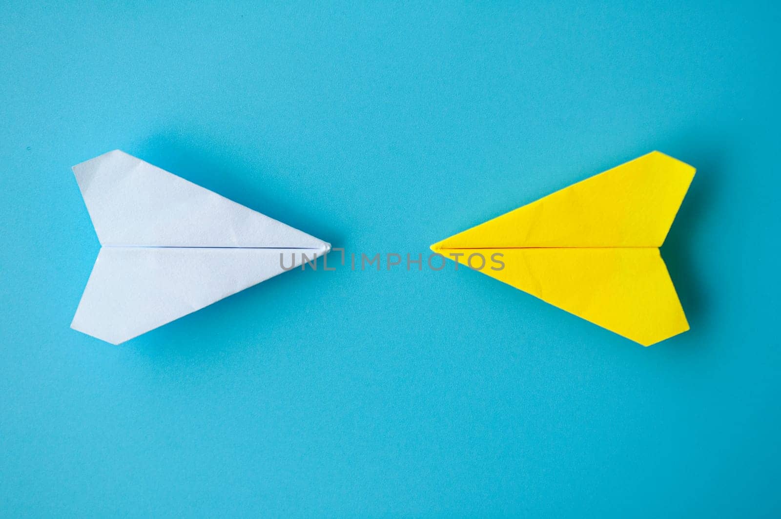 Top view of a white and yellow paper airplanes origami flying towards each other on blue background.