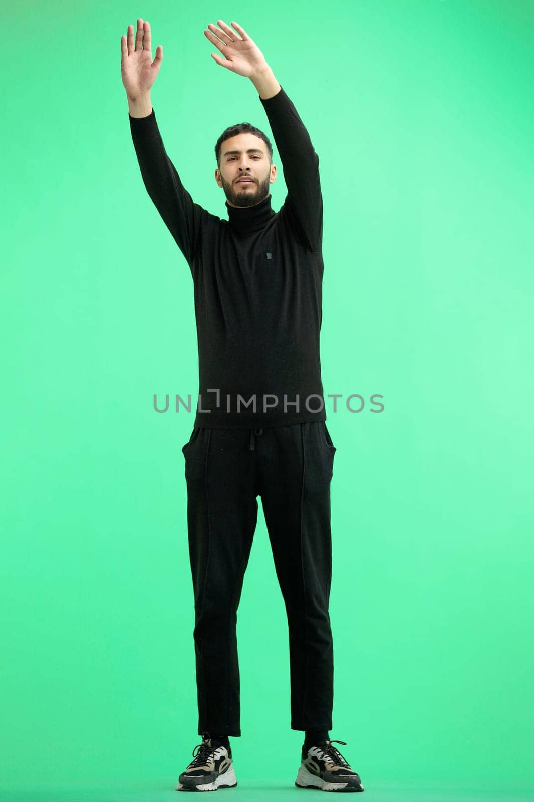 A man, full-length, on a green background, waving his arms.