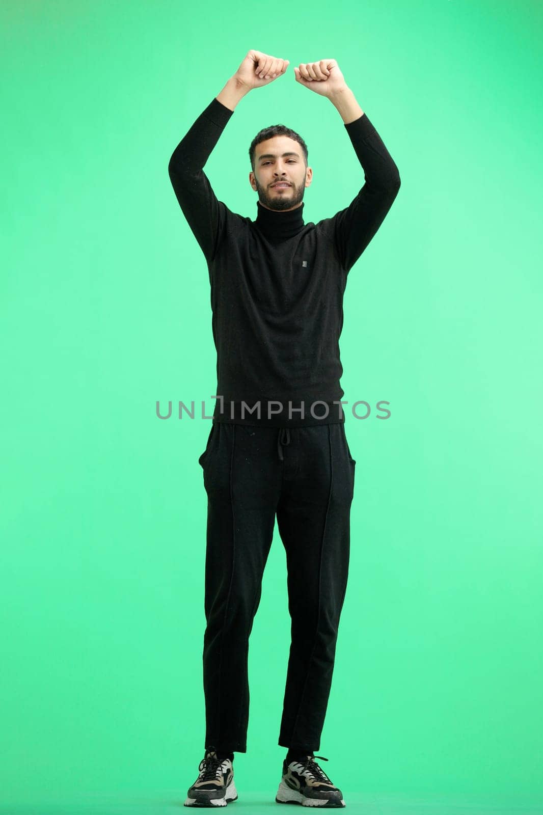 A man, full-length, on a green background, waving his arms.