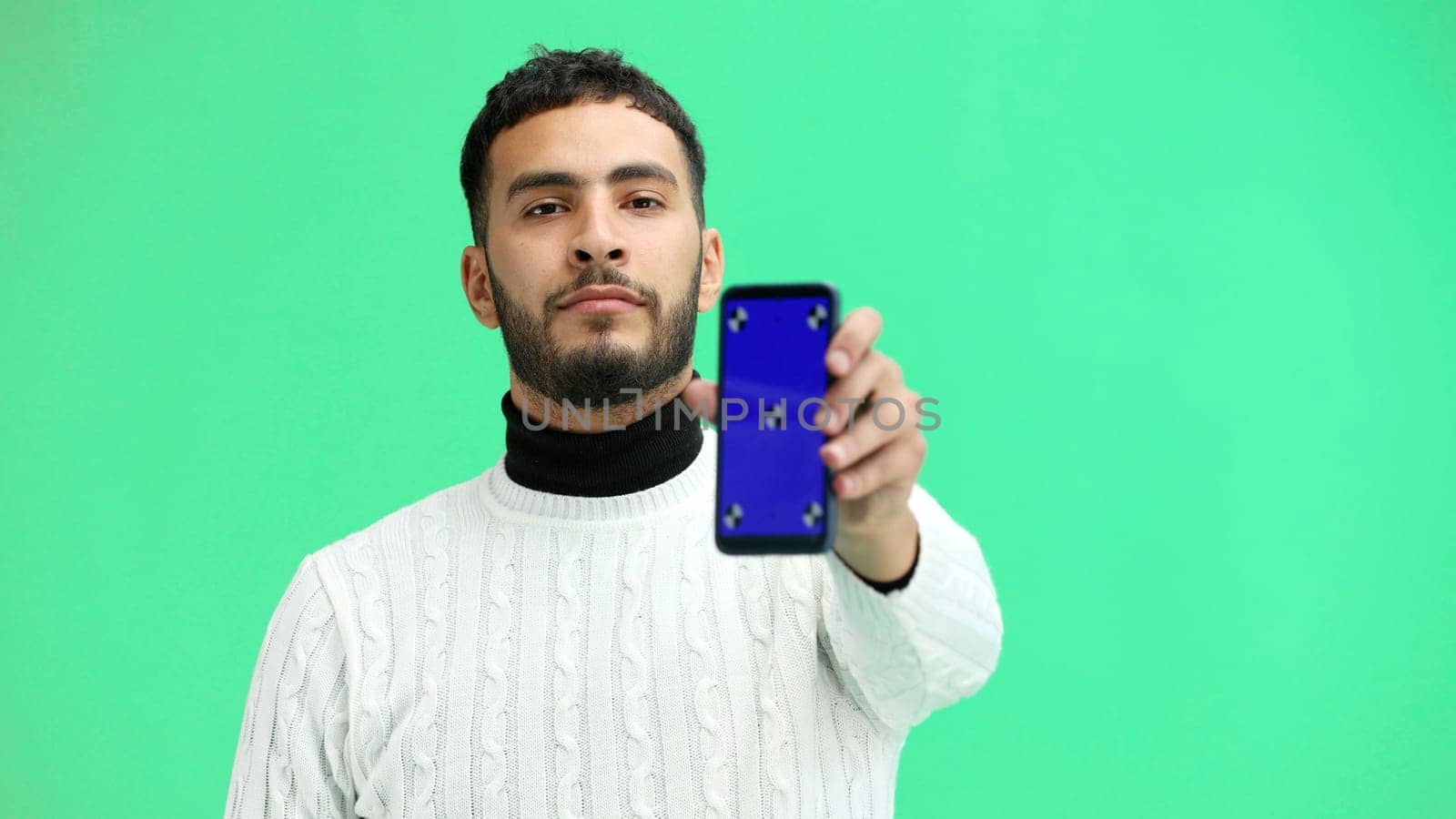 A man, close-up, on a green background, shows a phone.