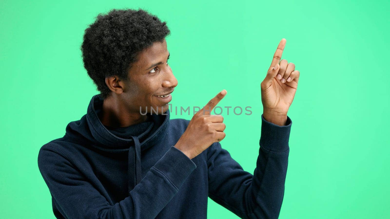 A man, close-up, on a green background, points to the side.