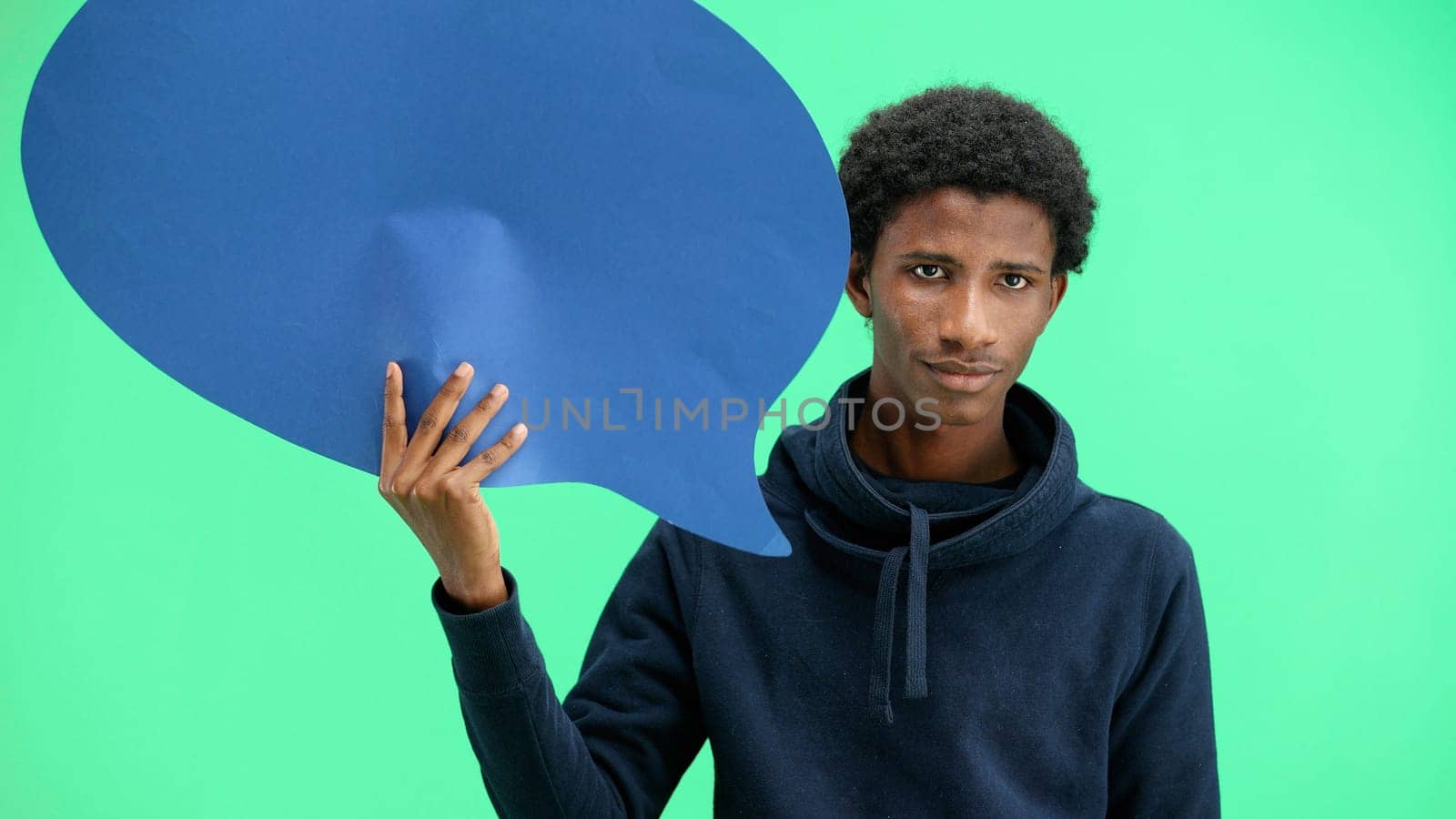 A man, close-up, on a green background, shows a blue comment sign.