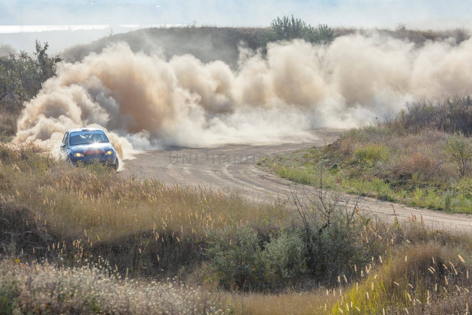 Sunny summer day. Dusty rally track. A rally car makes a lot of dust in a turn 16