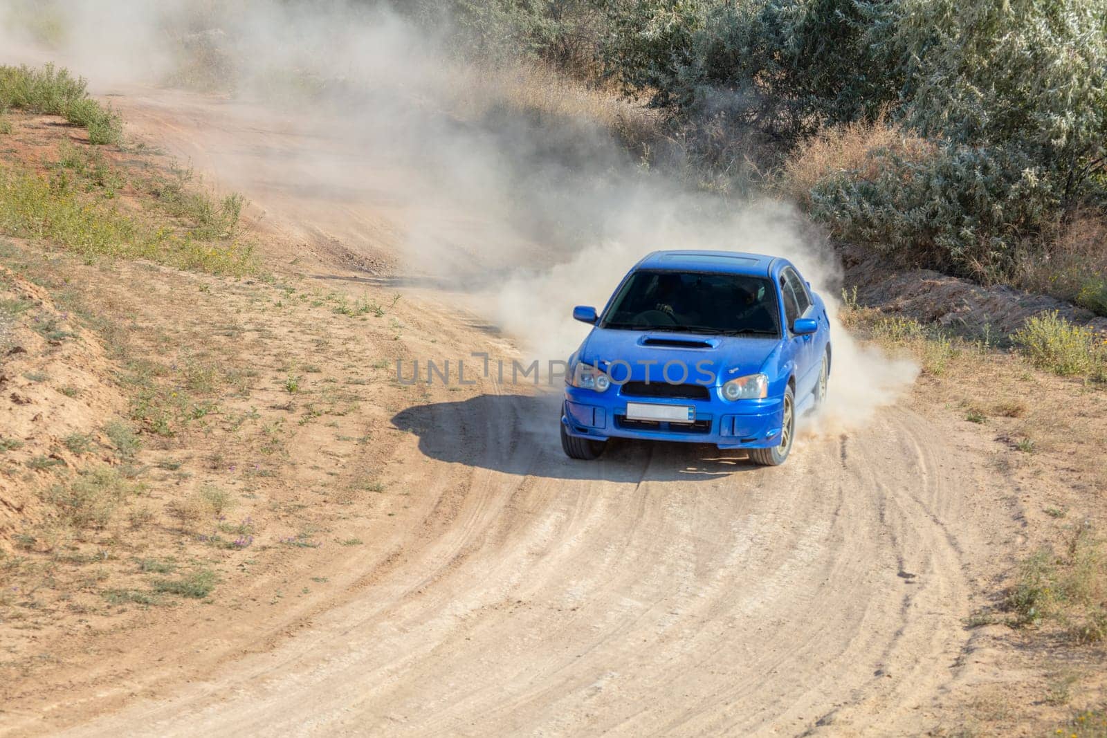 Sunny summer day. Dusty rally track. A rally car makes a lot of dust in a turn 12