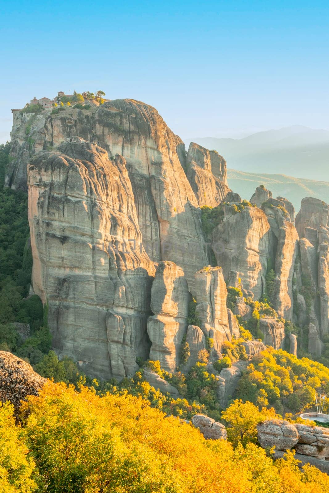 Greece. Bright sunny summer day in Kalambaka. A small rocky Greek monastery on a giant rock and vibrant vegetation in the foreground