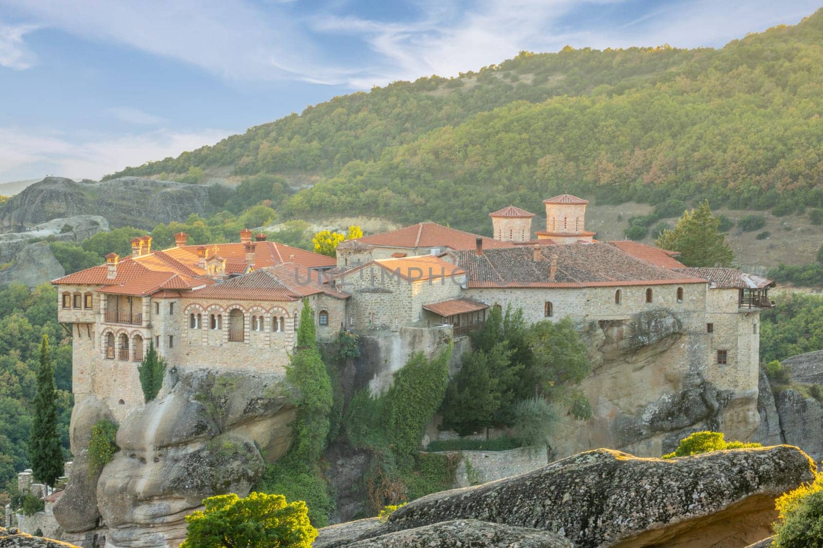 Greece. Early summer evening in Kalambaka. Rock monastery with red roofs and giant boulders in the foreground