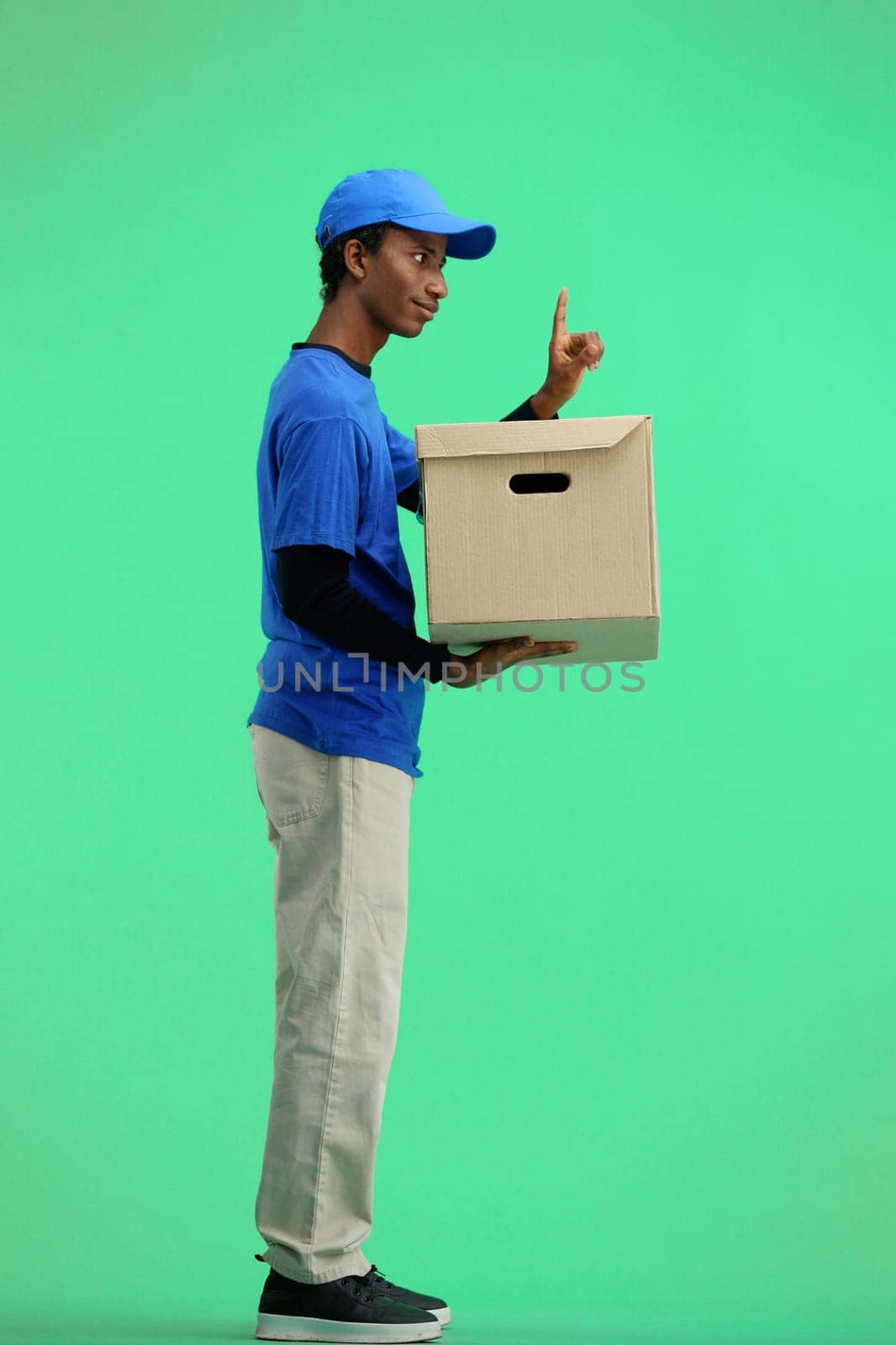 The deliveryman, in full height, on a green background, with a box, shows an important sign by Prosto