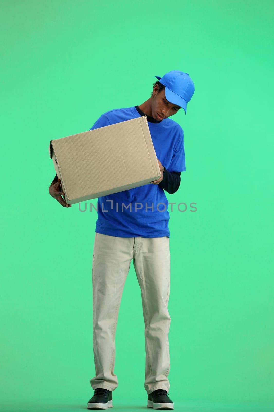 The deliveryman, in full height, on a green background, examines the box by Prosto
