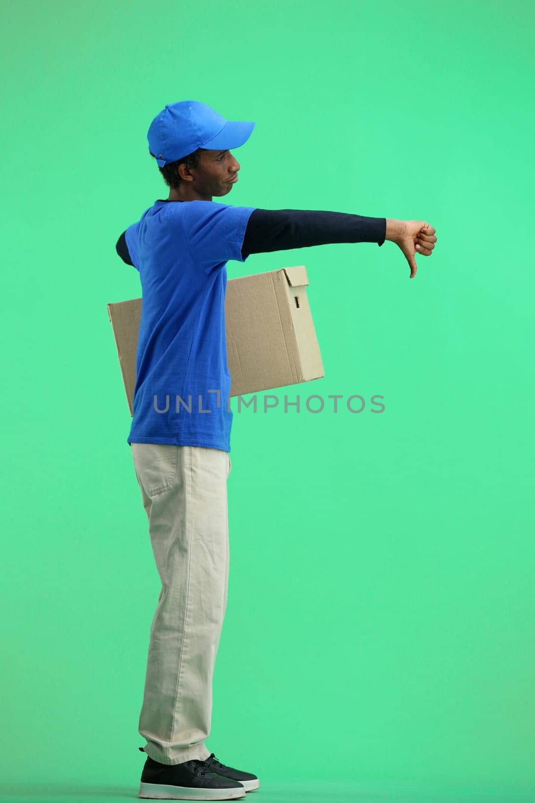 The deliveryman, in full height, on a green background, with a box, shows his finger down by Prosto