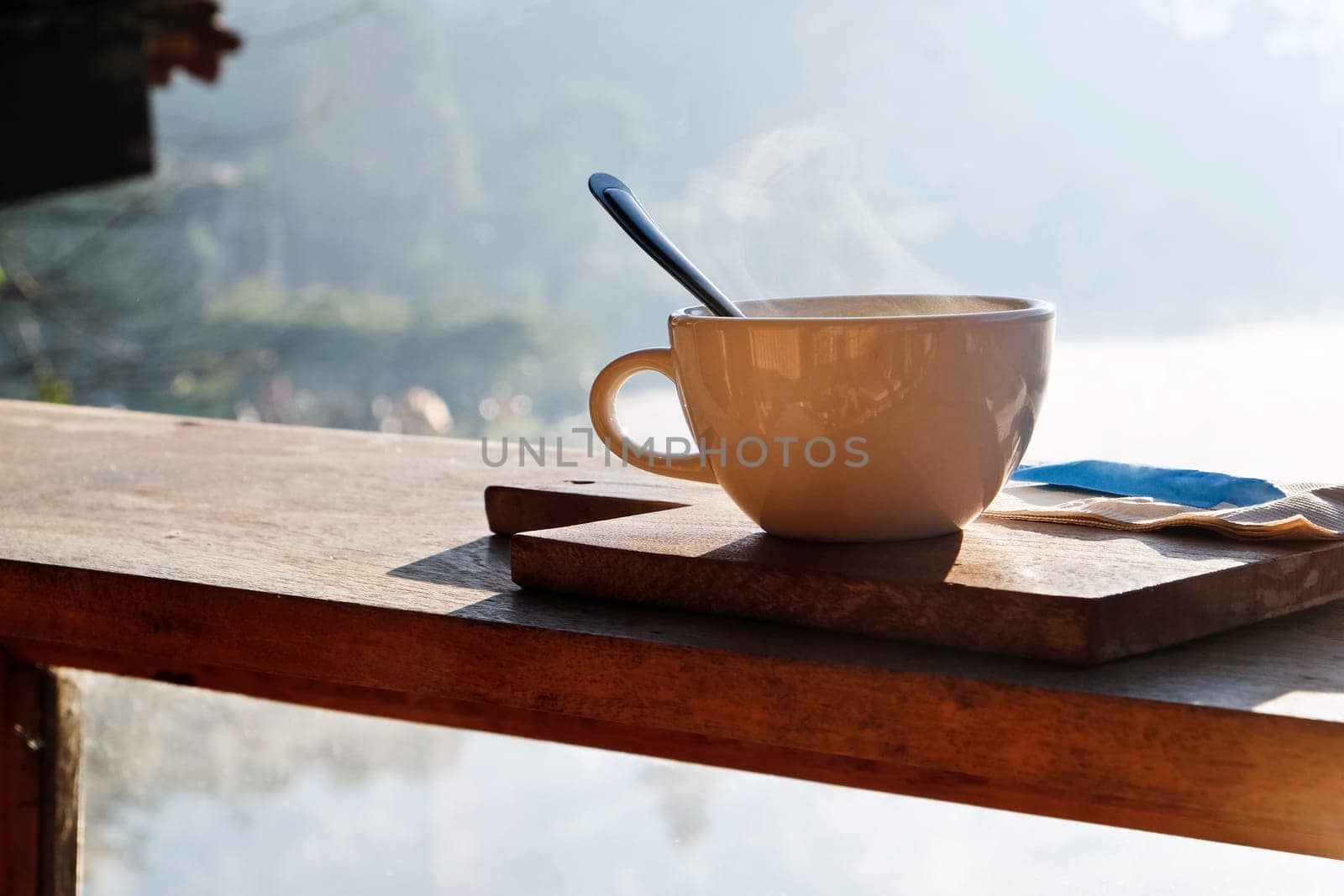 Coffee cup and napkin on wooden table in morning light by ponsulak