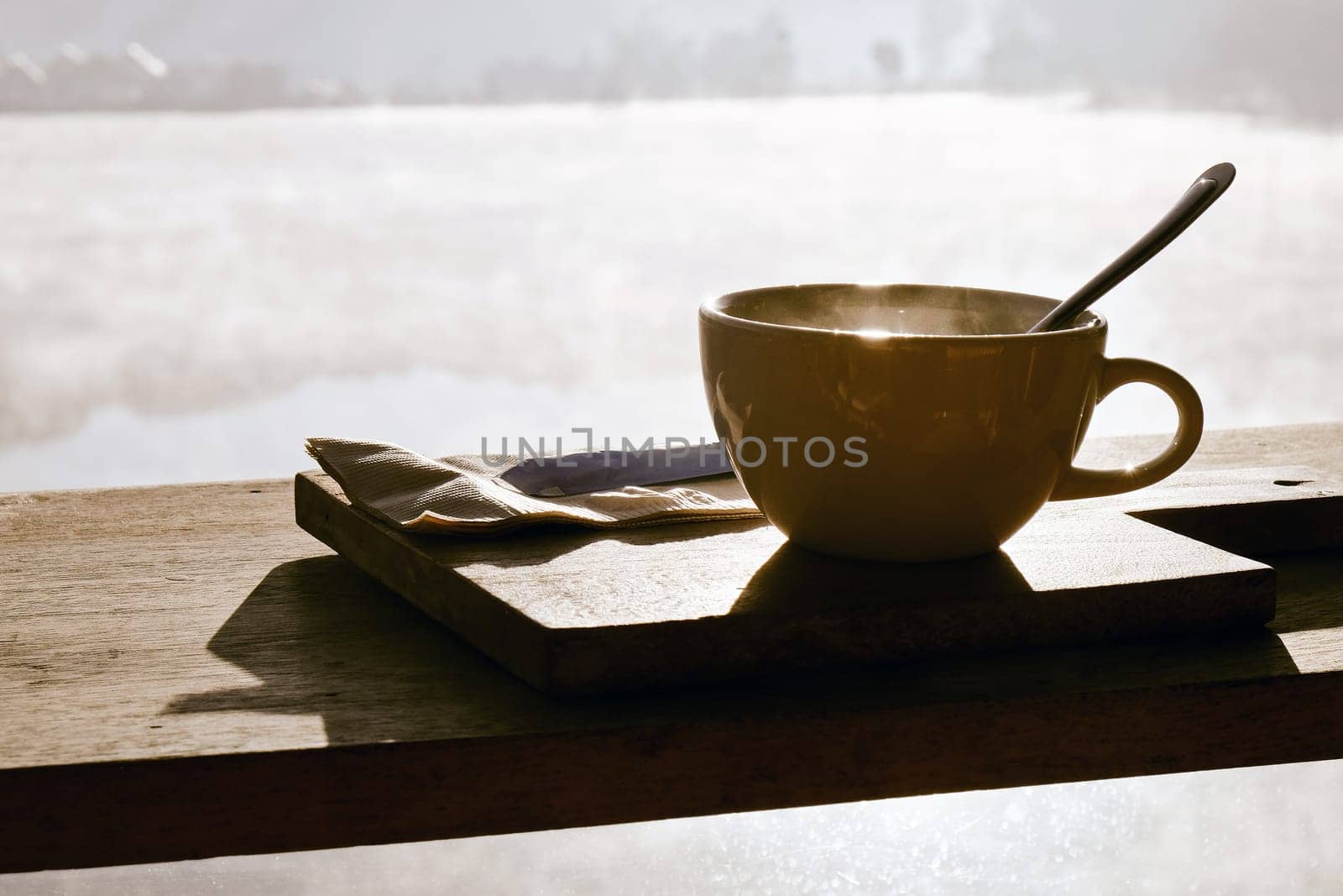 Coffee cup and napkin on wooden table in morning light by ponsulak