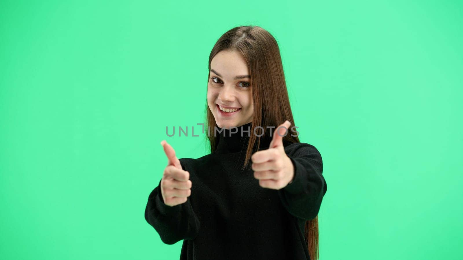 A woman, close-up, on a green background, shows her thumbs up.