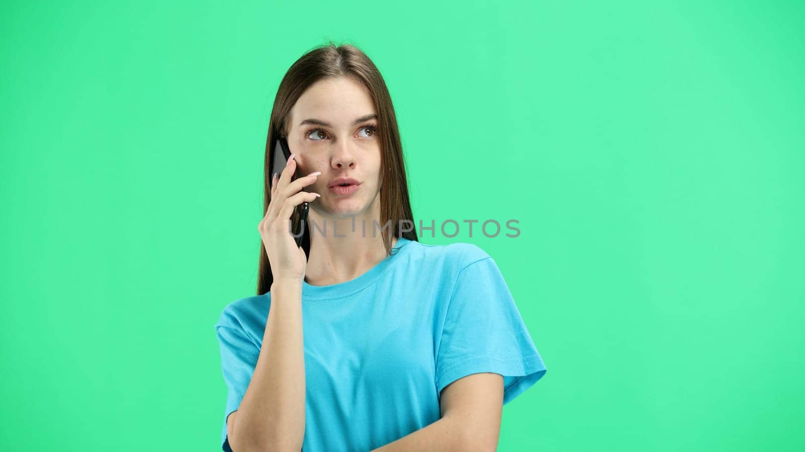 A woman, close-up, on a green background, talking on the phone.