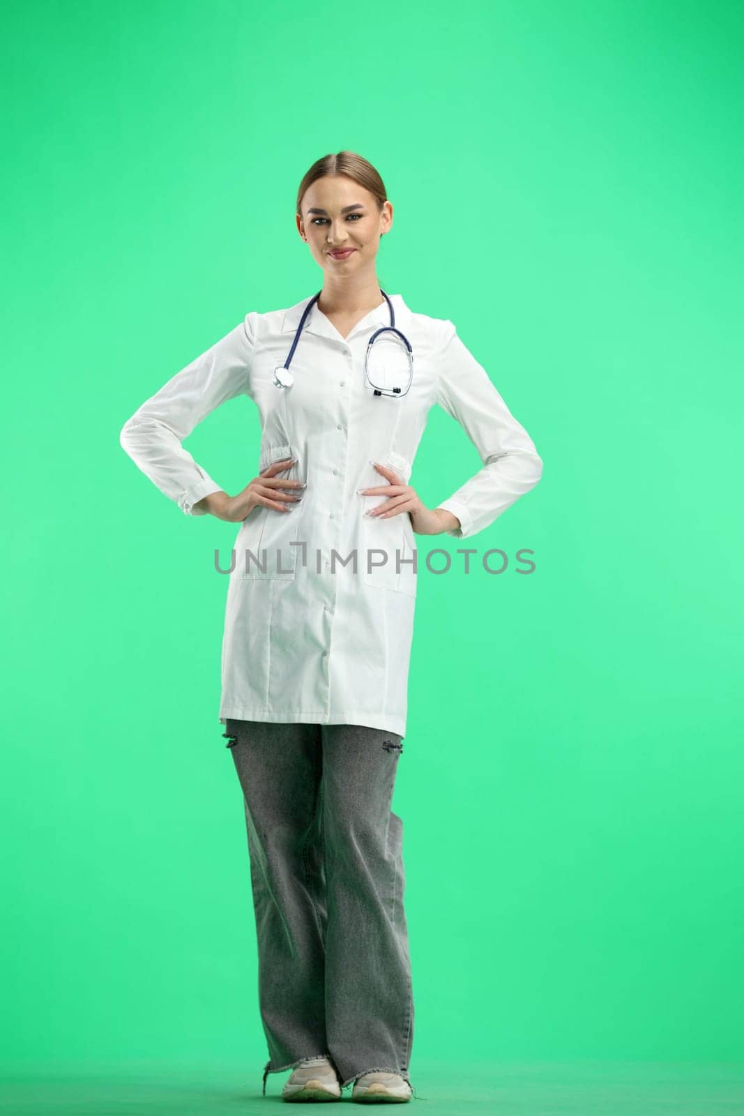 Female doctor, full-length, on a green background, hands on hips.