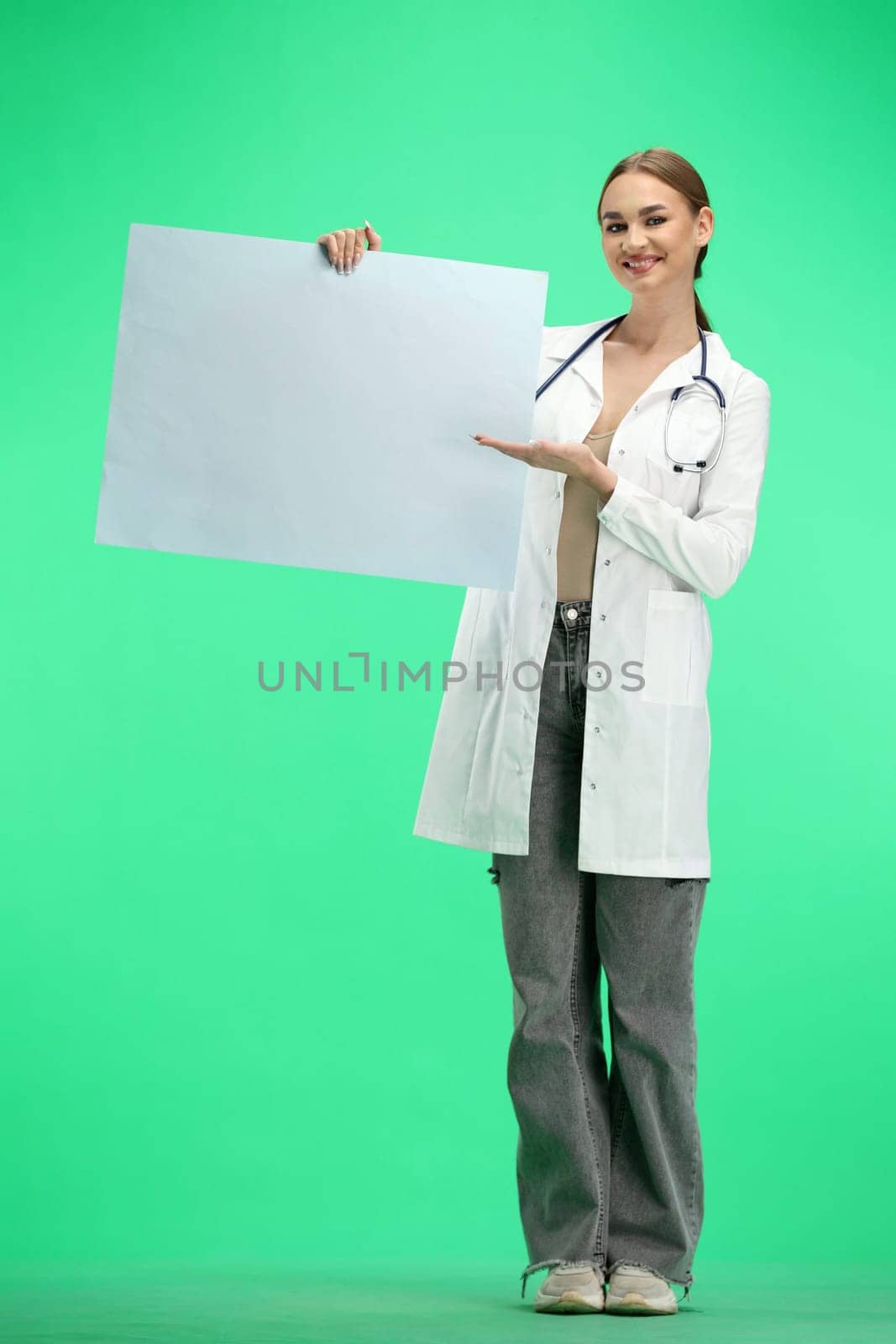 A female doctor, full-length, on a green background, shows a white sheet.