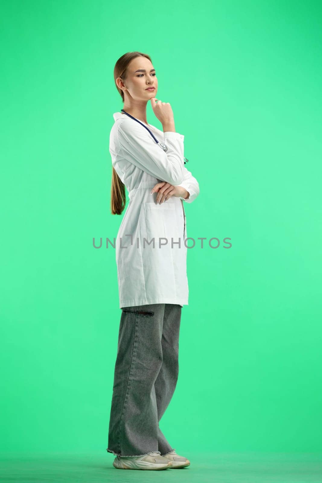 A woman doctor, full-length, on a green background, thinks.