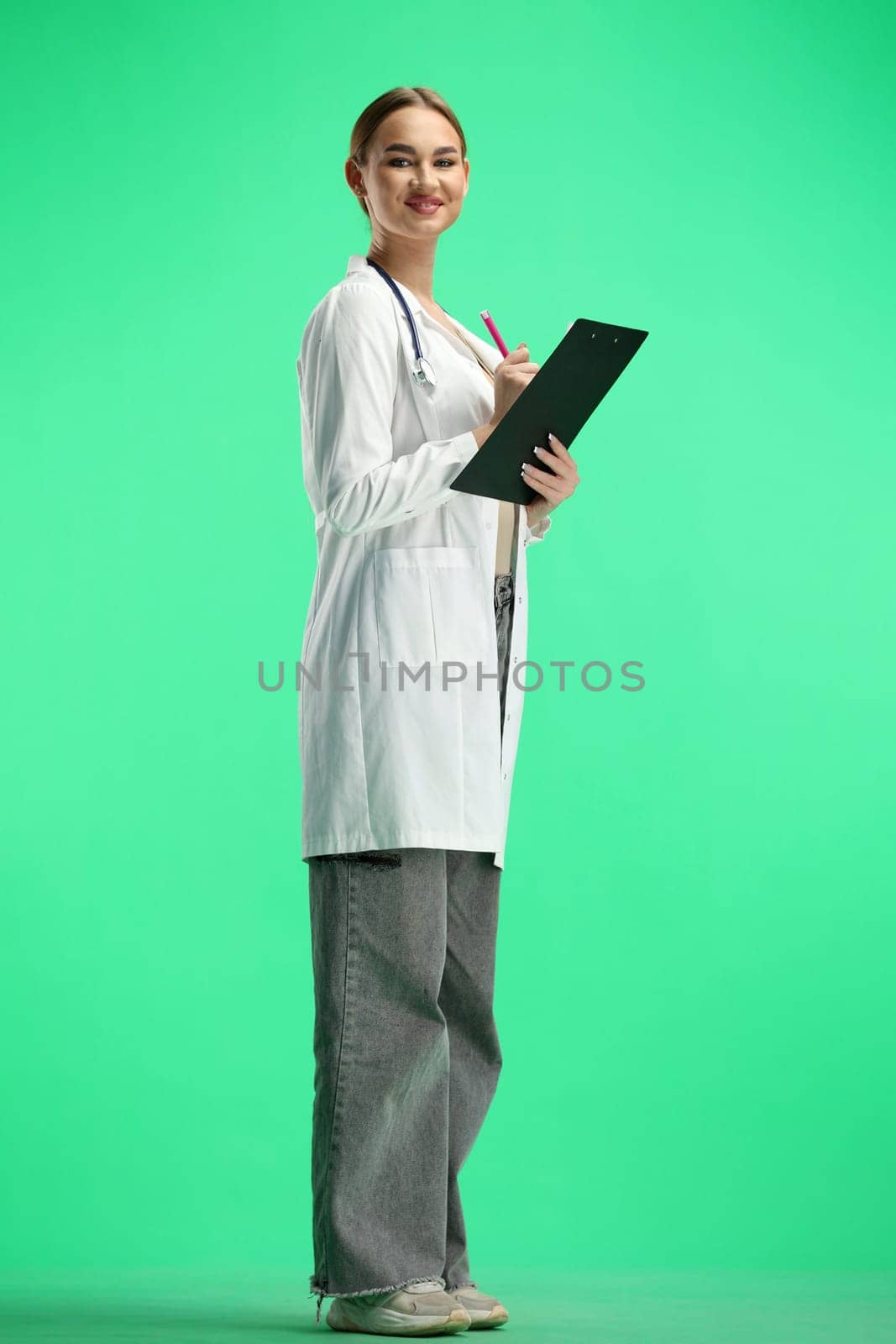 A woman doctor, full-length, on a green background, writes.