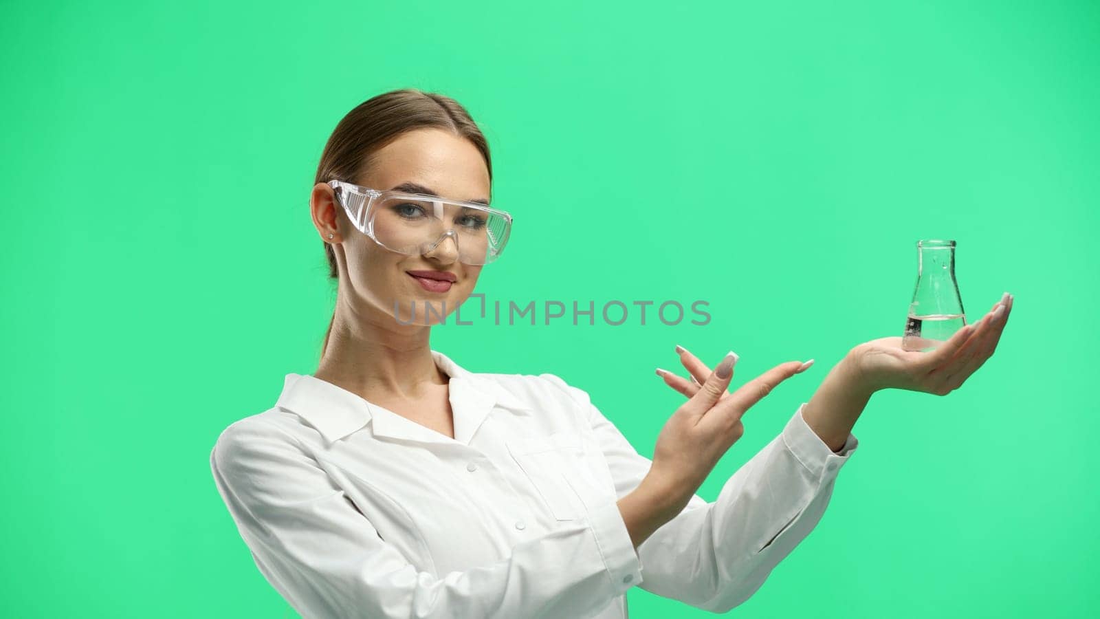 Female doctor, close-up, on a green background, holding a bottle.