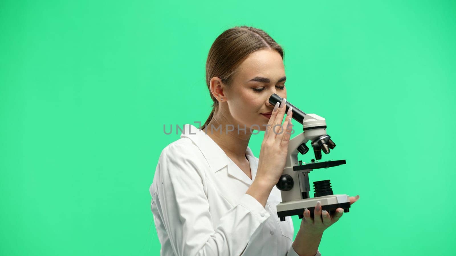 Female doctor, close-up, on a green background, with a microscope.