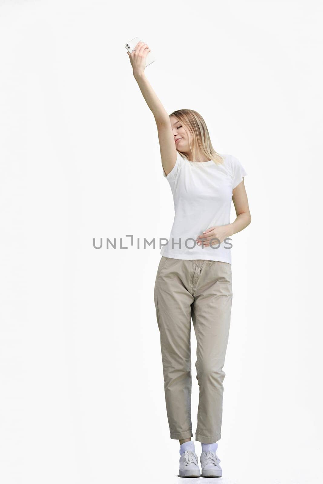 A woman, full-length, on a white background, waving her phone.