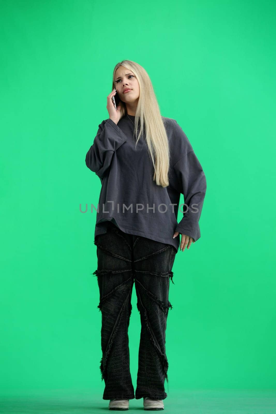 A woman, full-length, on a green background, talking on the phone.