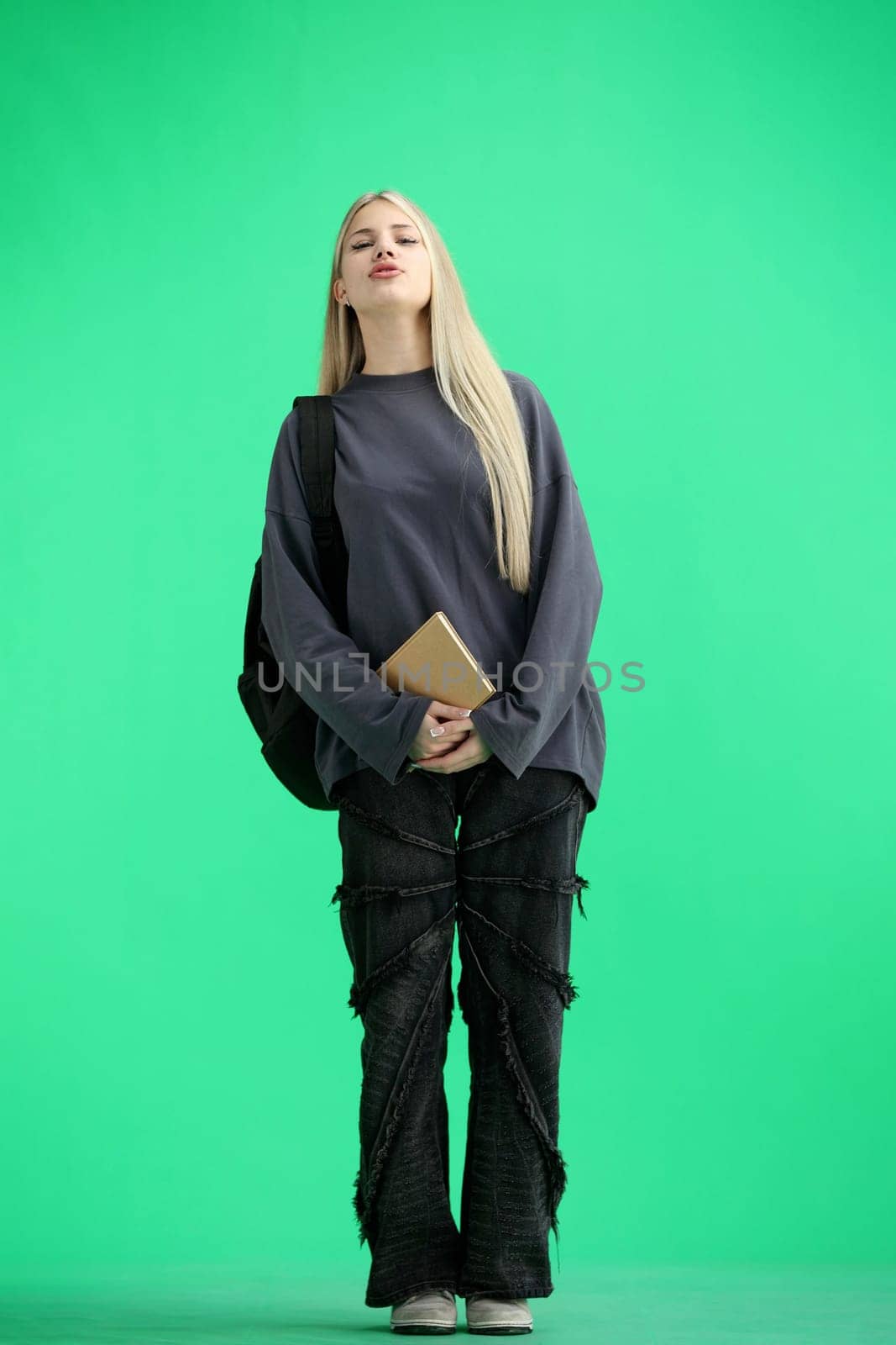 A woman, full-length, on a green background, with a backpack.