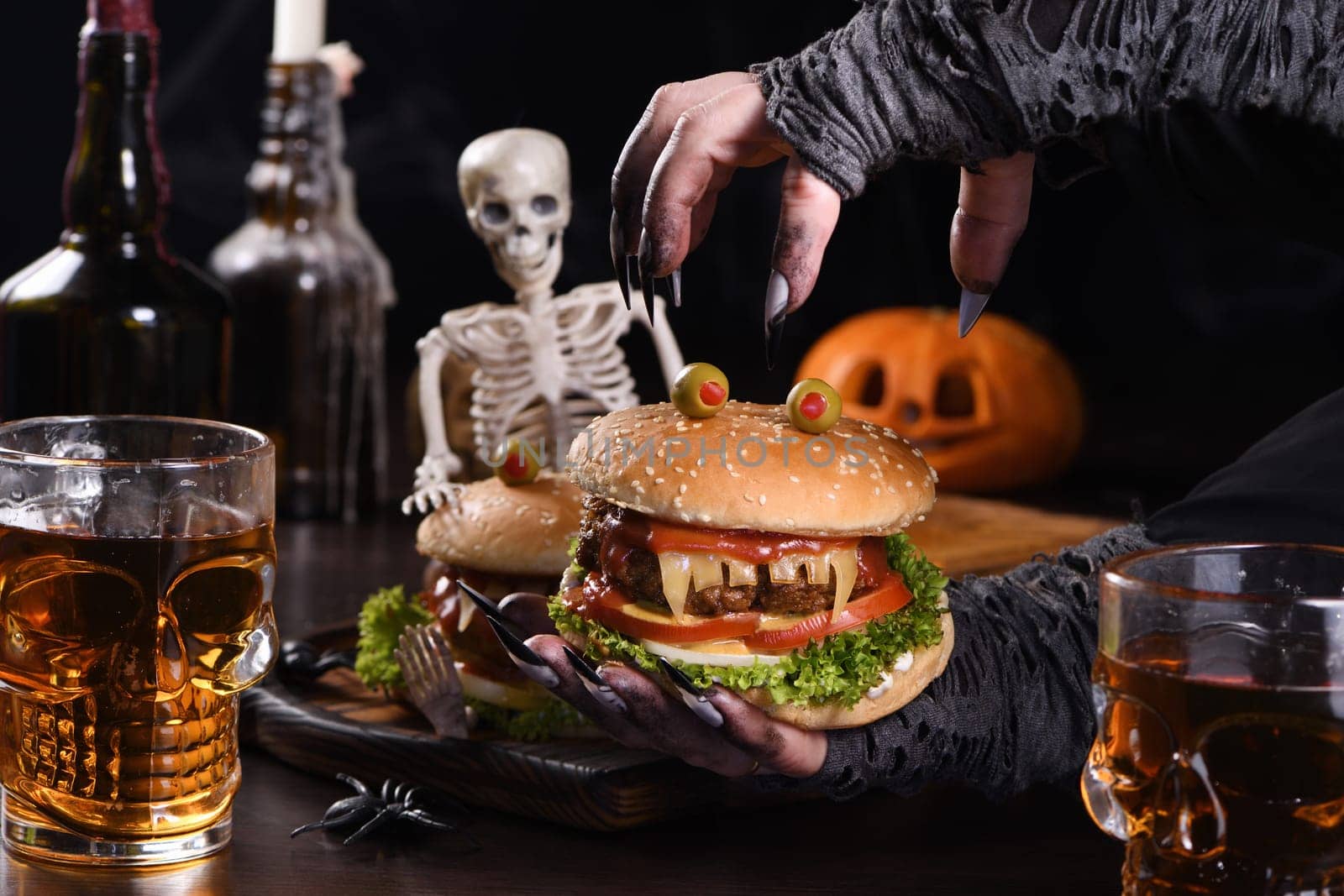The witches hands hold a Monster Burger in her palms on a sitting skeleton. Perfect Halloween Party appetizer