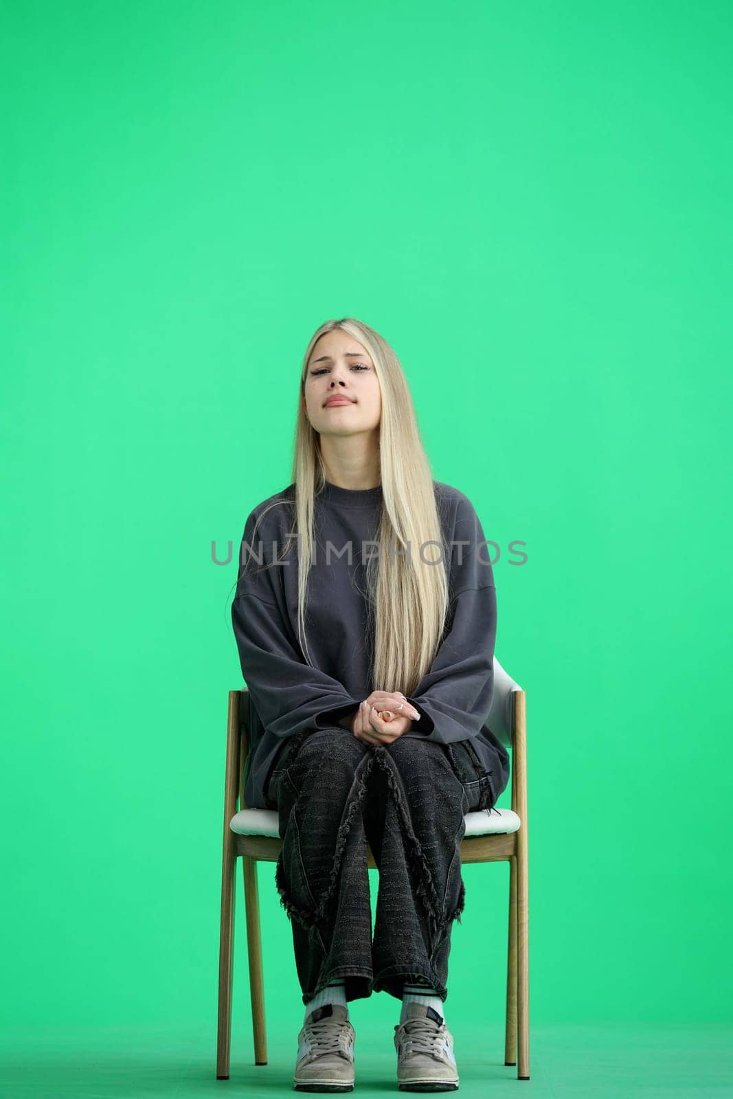 A woman, full-length, on a green background, sitting on a chair.