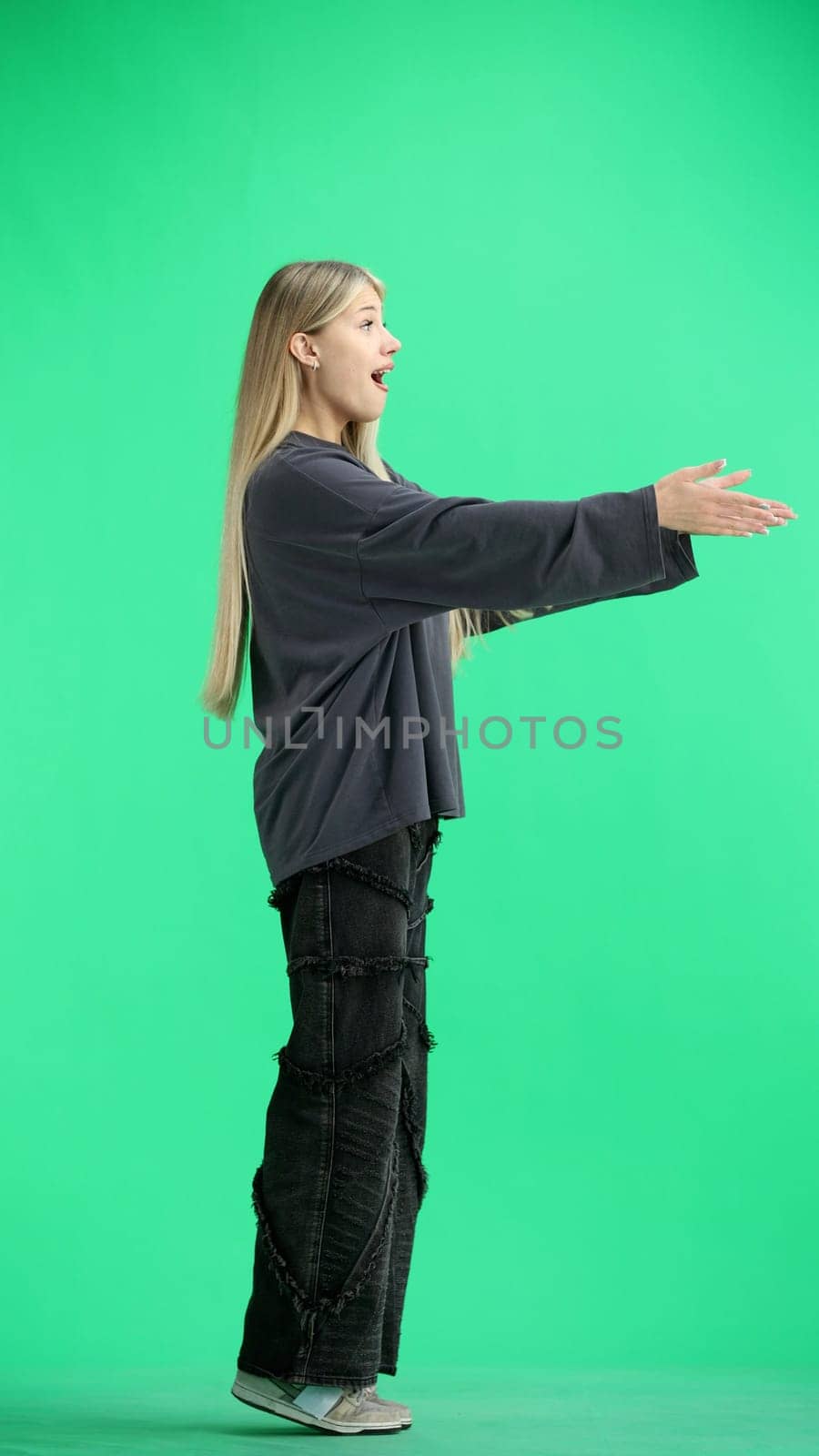 A woman, full-length, on a green background, spreads her arms.