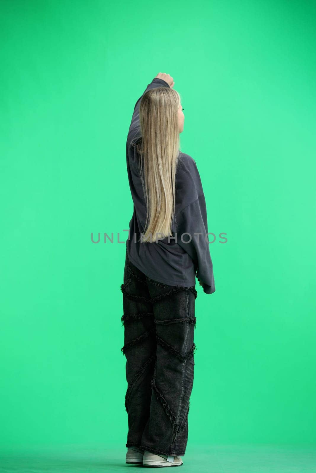 A woman, full-length, on a green background, raised her hand up.