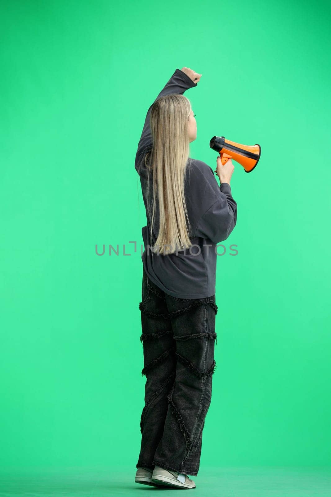 A woman, full-length, on a green background, with a megaphone.