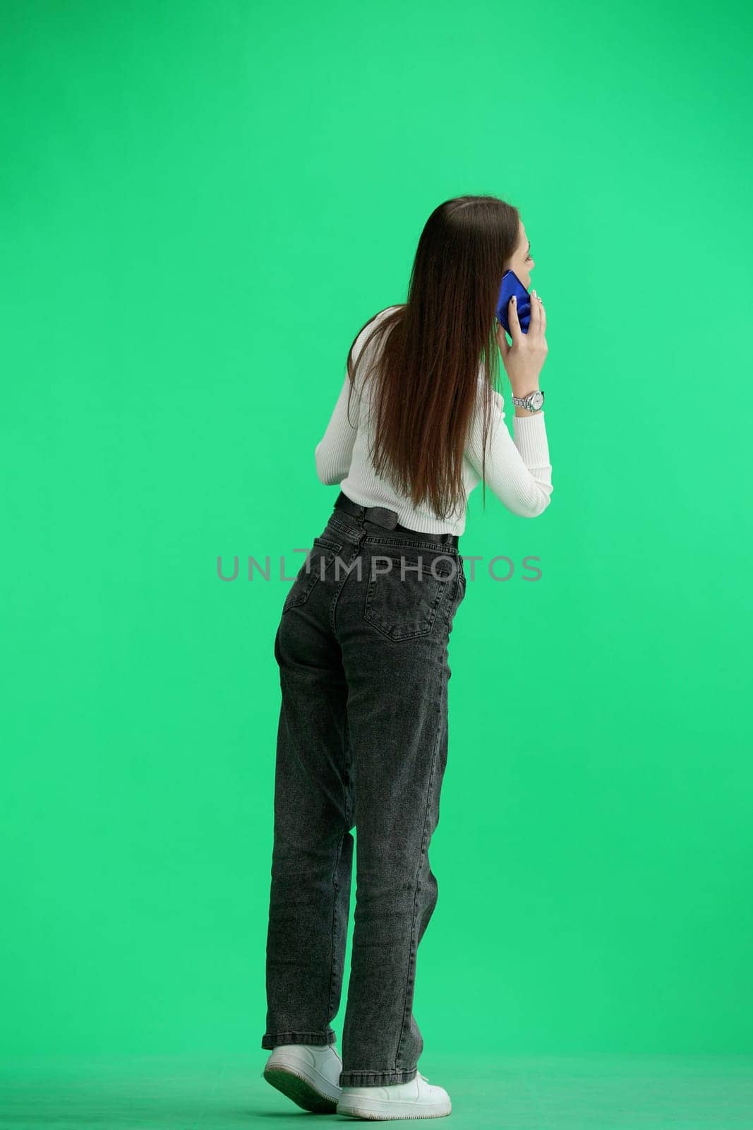 A woman, full-length, on a green background, talking on the phone.
