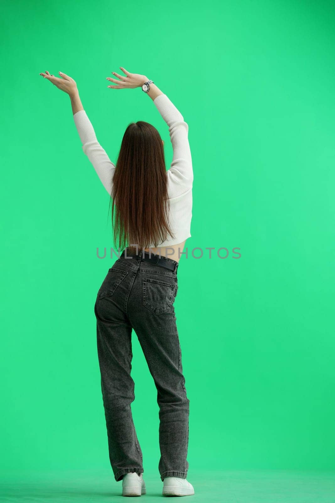 A woman, full-length, on a green background, waving her arms.