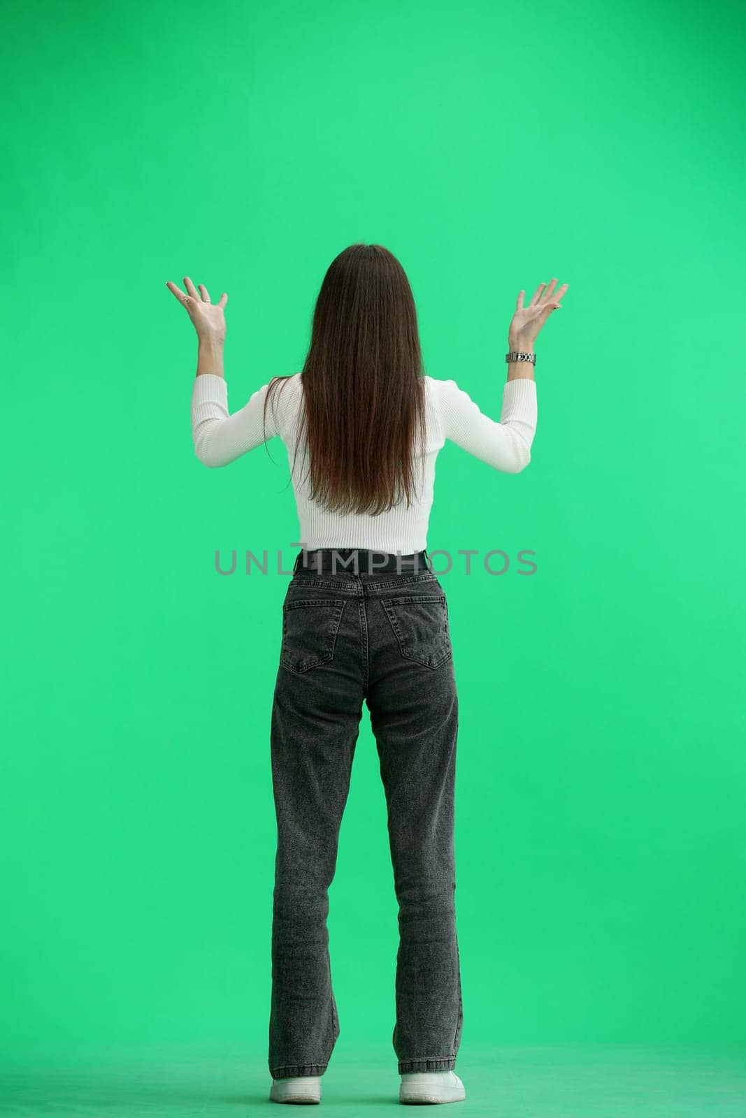 A woman, full-length, on a green background, spreads her arms.