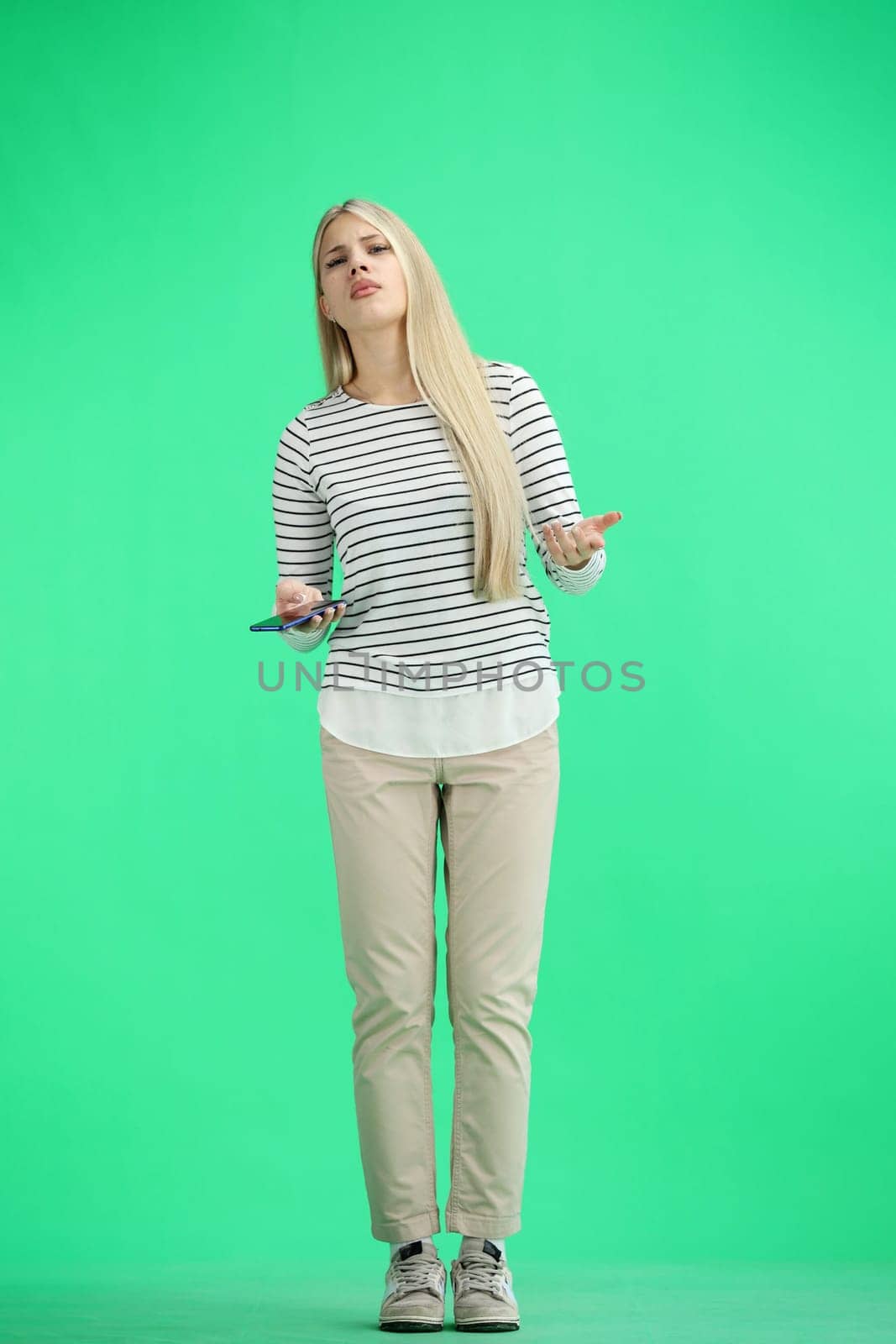 A woman, full-length, on a green background, uses a phone.