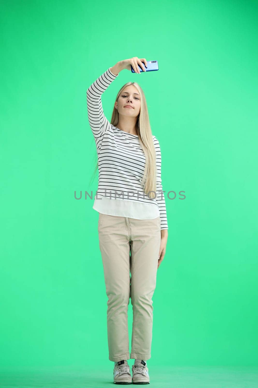 A woman, full-length, on a green background, waving her phone.