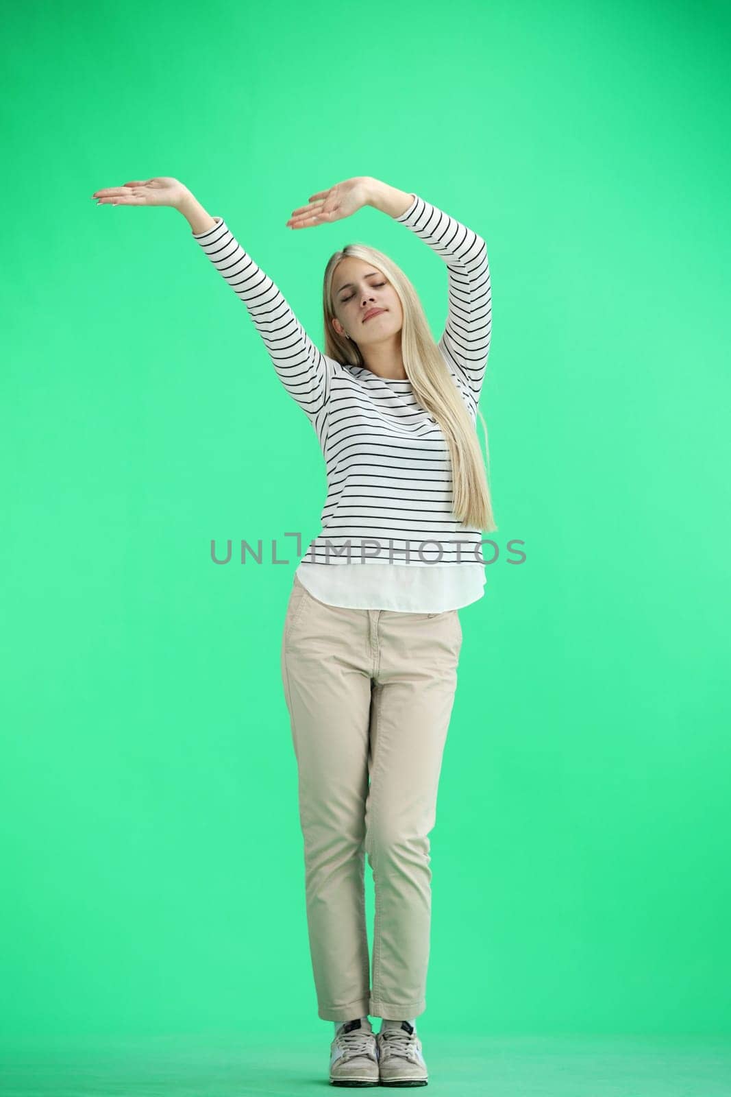 A woman, full-length, on a green background, waving her arms.
