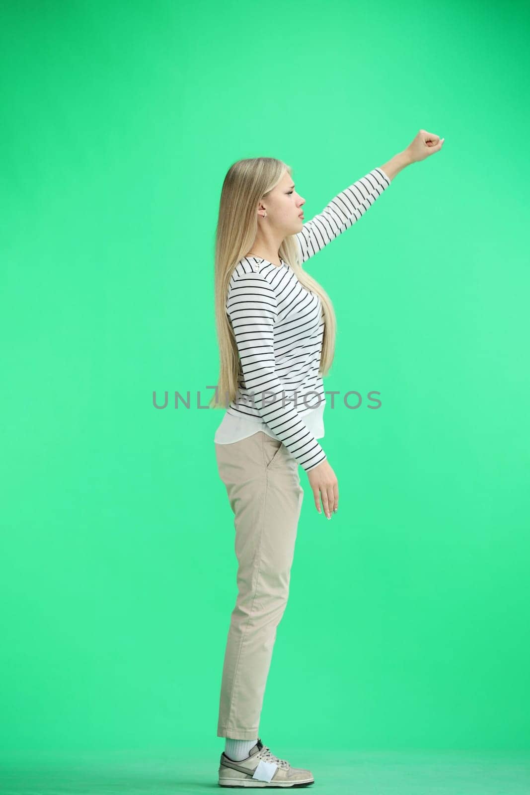 A woman, full-length, on a green background, raised her hand up.