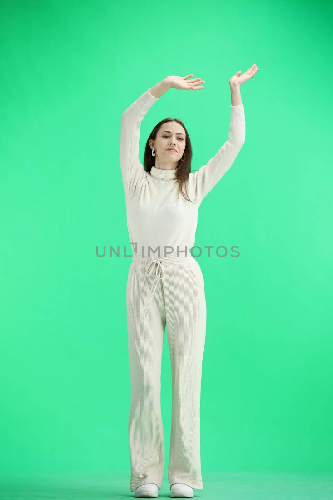 A woman, full-length, on a green background, waving her arms.