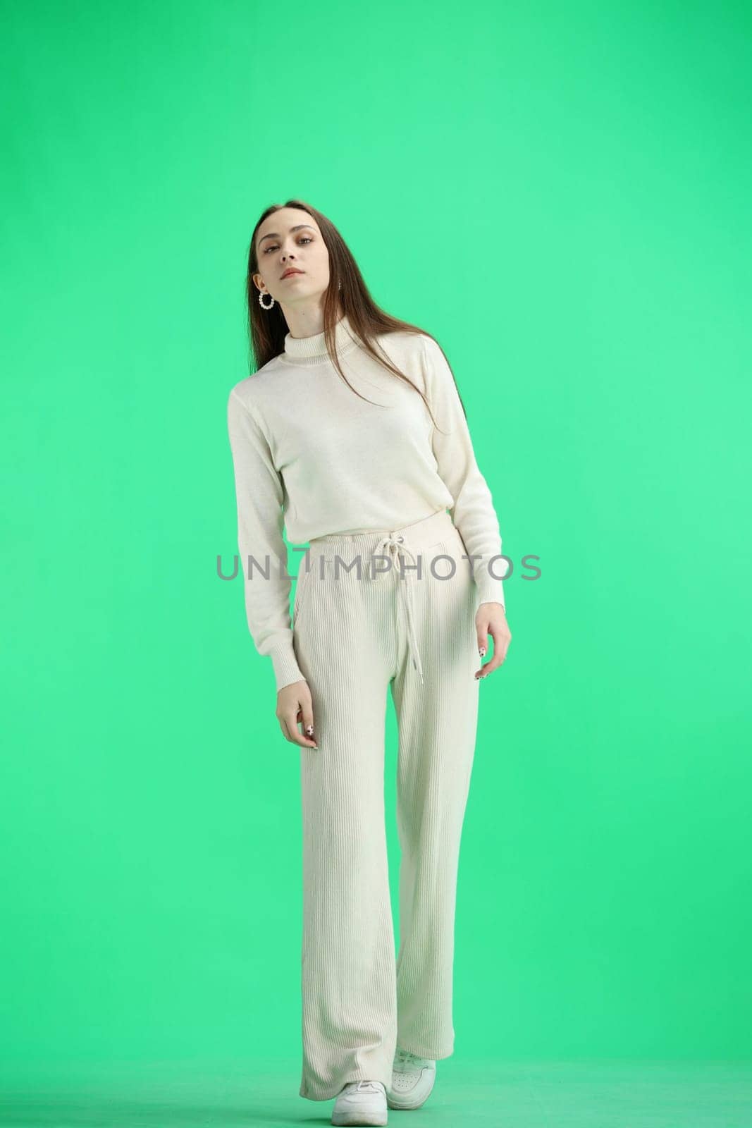 A woman, full-length, on a green background, looks into the distance.