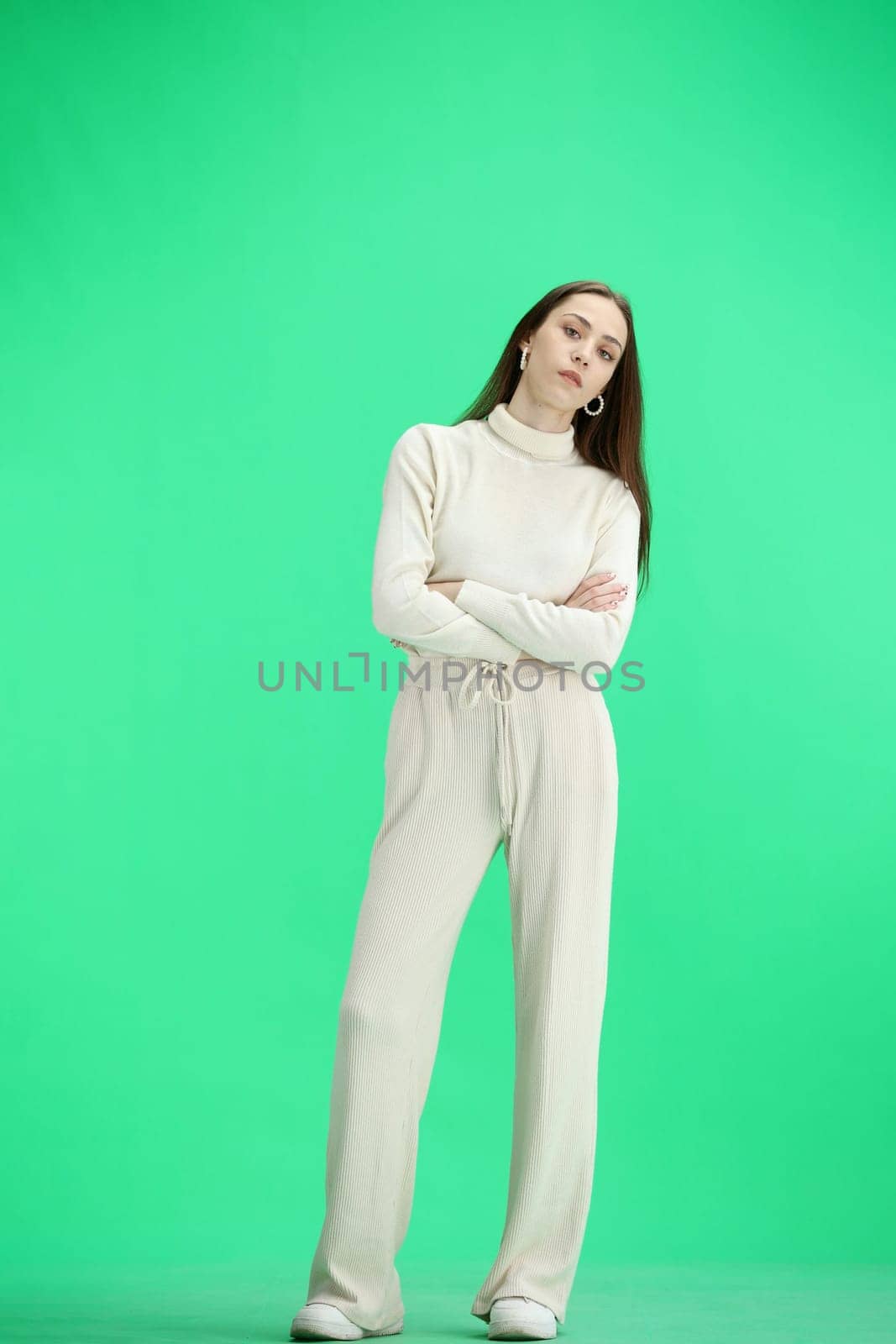 A woman, full-length, on a green background, crossed her arms.