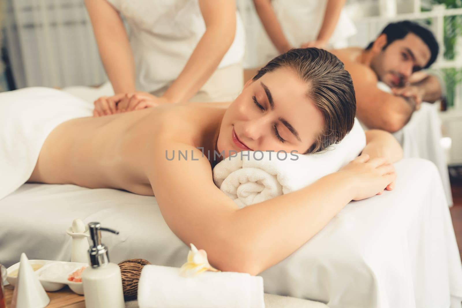 Caucasian couple customer enjoying relaxing anti-stress spa massage and pampering with beauty skin recreation leisure in day light ambient salon spa at luxury resort or hotel. Quiescent