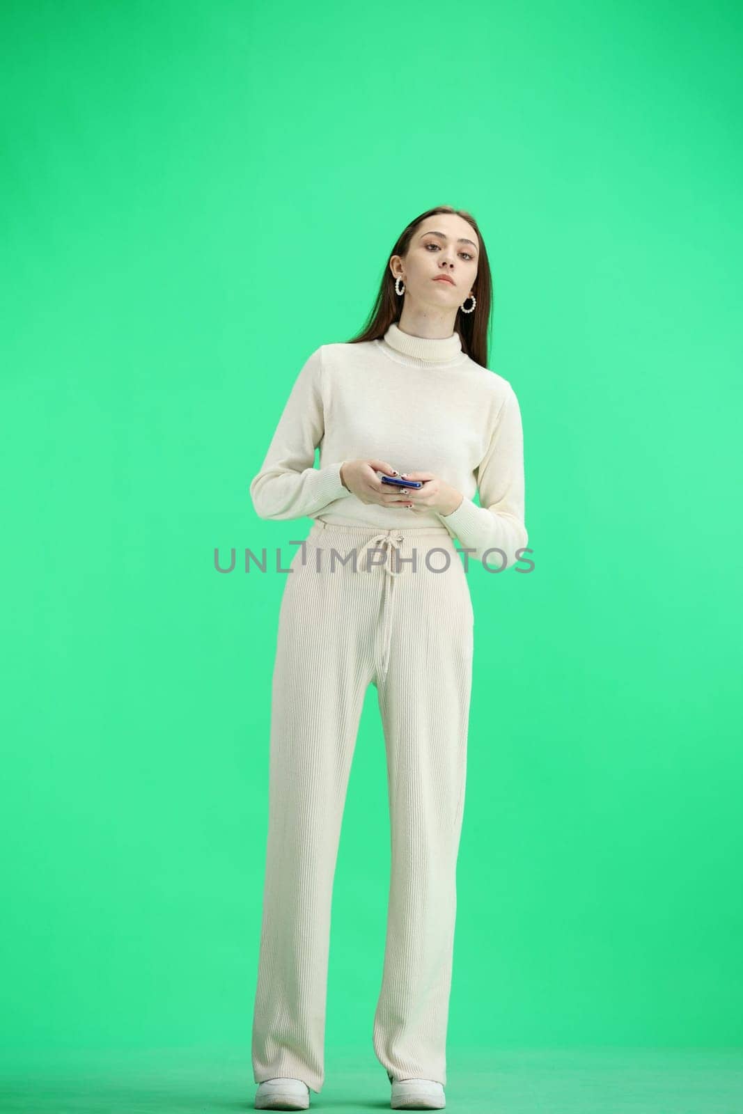 A woman, full-length, on a green background, uses a phone.