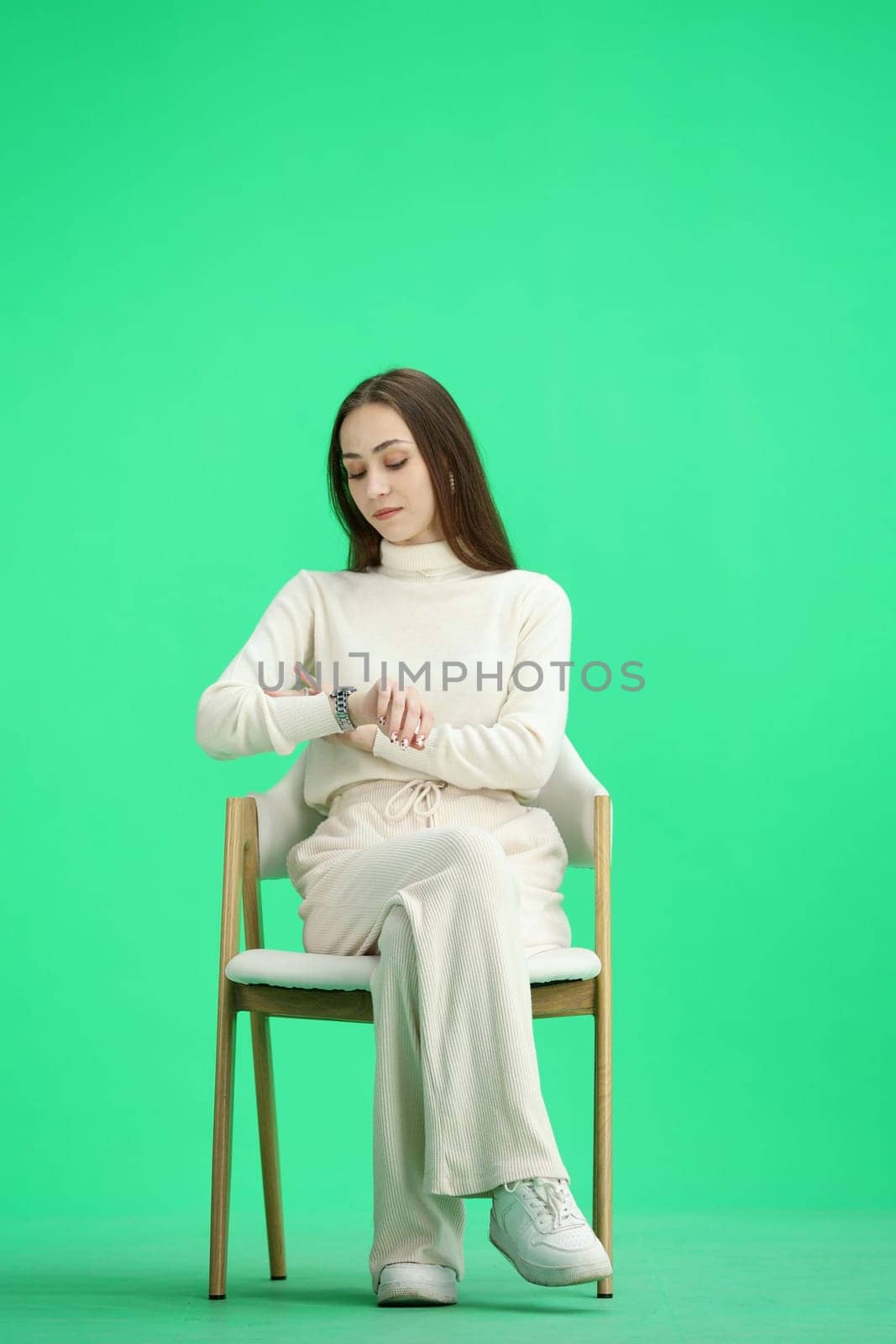 A woman, full-length, on a green background, sitting on a chair.