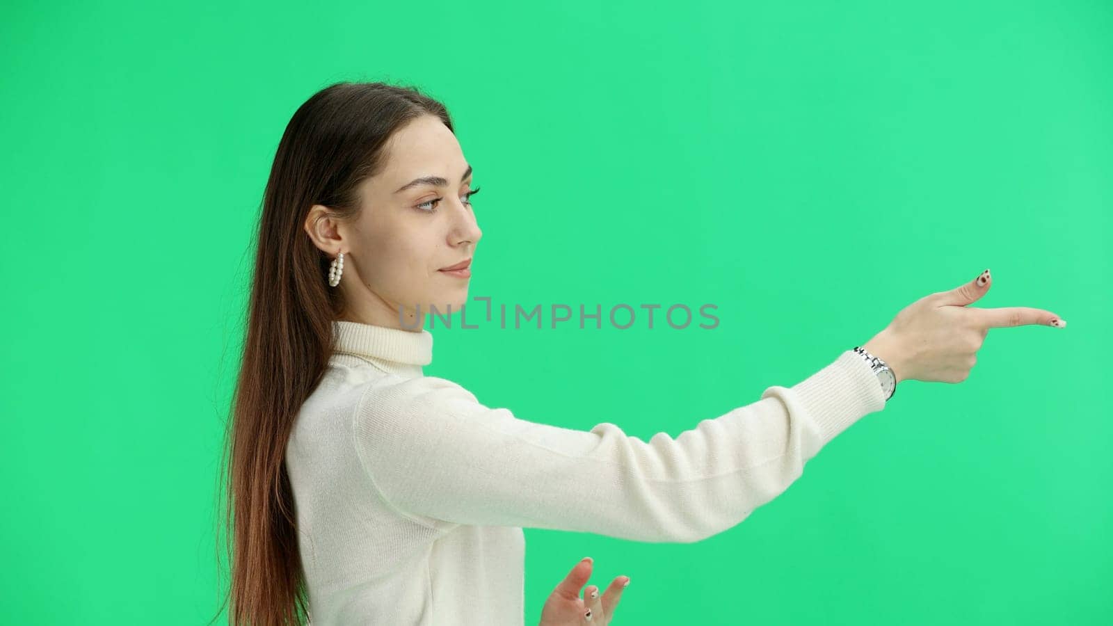 A woman, close-up, on a green background, points to the side.