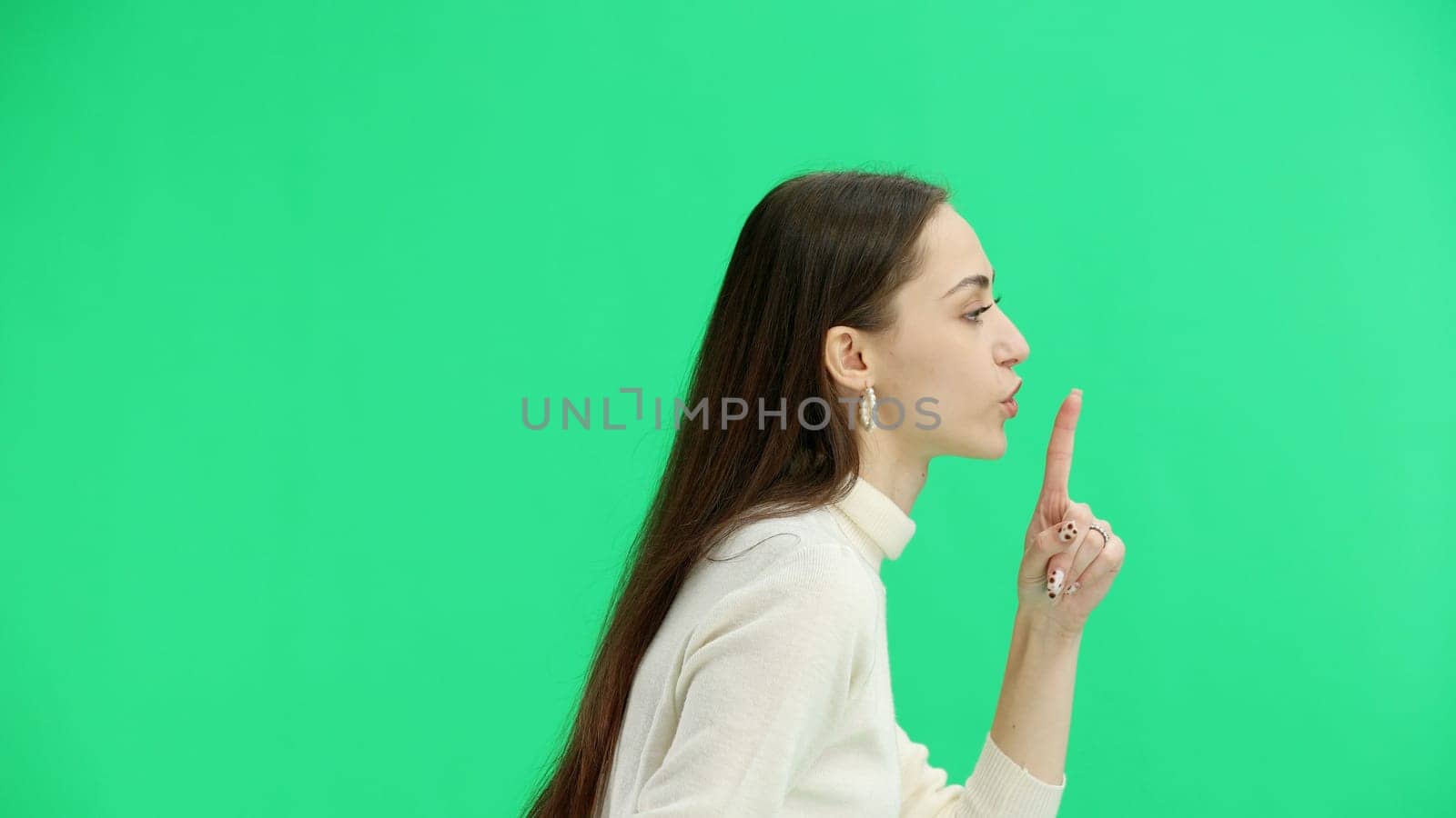 A woman, close-up, on a green background, shows a sign of silence.