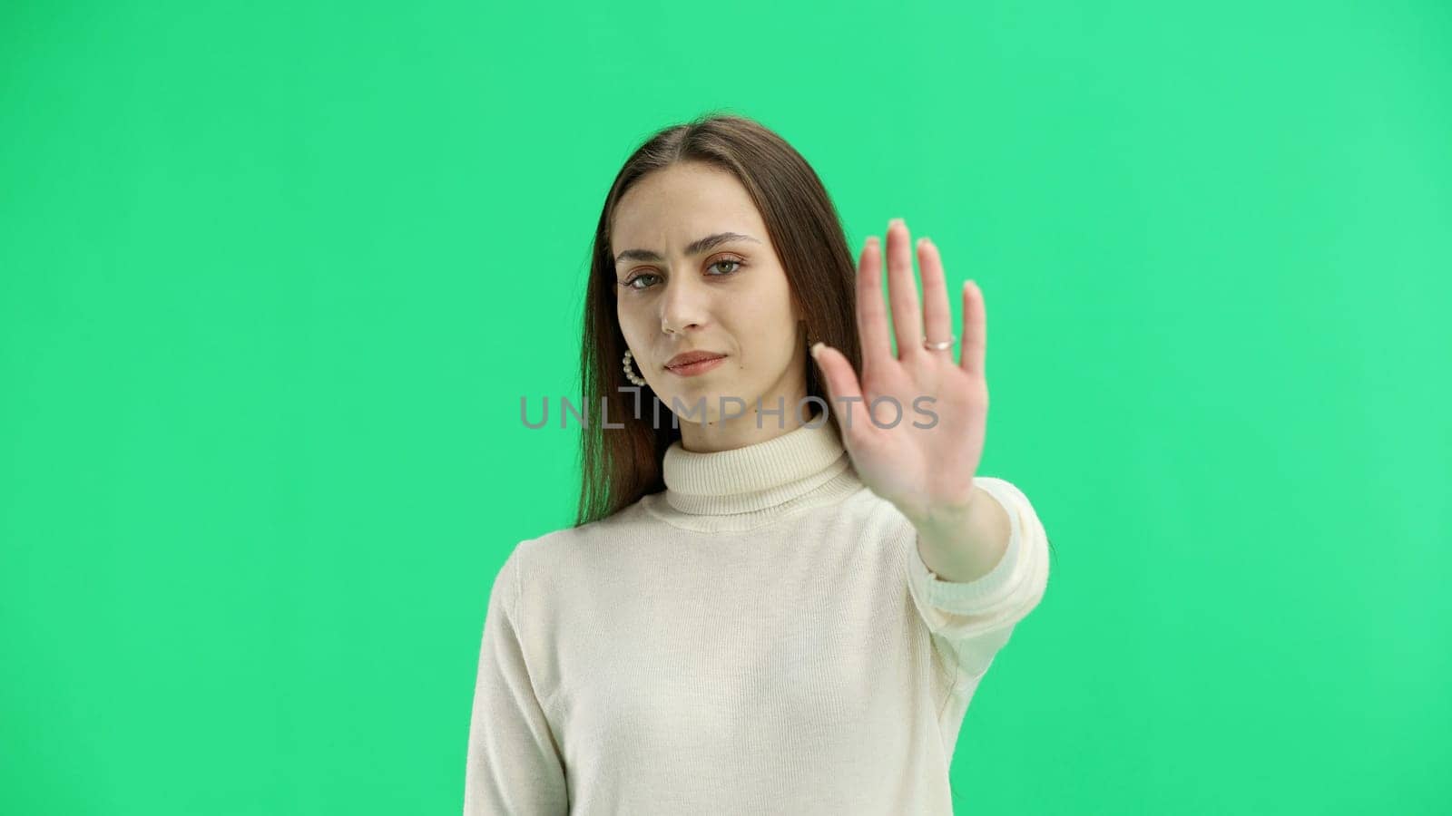 A woman, close-up, on a green background, shows a stop sign.