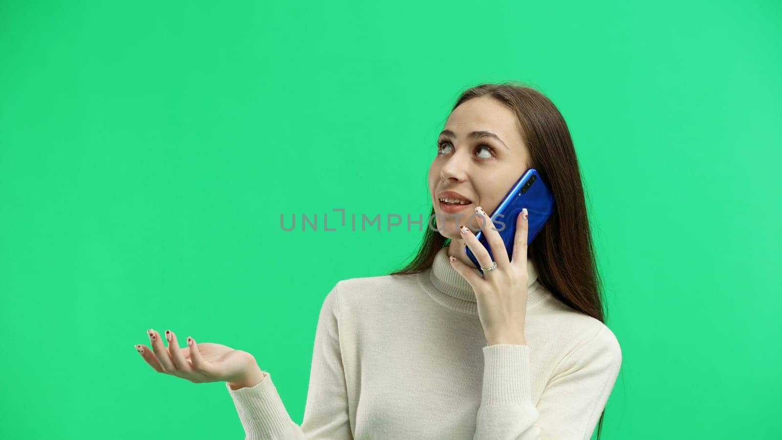 A woman, close-up, on a green background, talking on the phone.